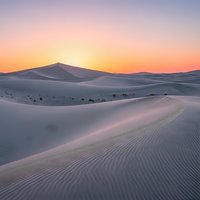 Desert sand dunes at sunrise with golden sky and rippled texture patterns creating serene landscape for travel and nature backgrounds.