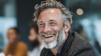 Happy mature Caucasian businessman with gray beard laughing in modern office environment for corporate communication and professional success concepts.