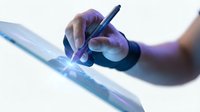 Professional artist hand holding stylus pen drawing on digital tablet screen with blue light effects for creative design work and digital art projects.