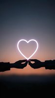 Silhouetted hands holding glowing neon heart shape against dusky sky background, creating romantic atmosphere for valentines, love and relationship concepts.