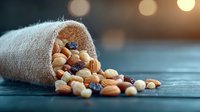 Mixed nuts and dried berries spilling from rustic burlap sack onto dark wooden surface with warm bokeh lights in background, creating cozy food composition.