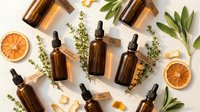 Natural organic skincare products with amber glass dropper bottles, dried orange slices and fresh herbs on white background for wellness branding.