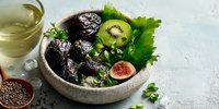 Fresh healthy salad bowl with dates, kiwi, figs and greens served with herbal tea on marble surface for nutritious meal planning.