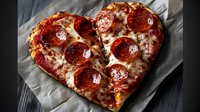 Heart shaped pepperoni pizza with melted mozzarella cheese on baking paper against dark wooden background, romantic dinner concept for Valentine's day celebration.
