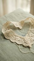Vintage cream lace collar with delicate floral pattern on soft green fabric, romantic feminine fashion accessory for handmade clothing and sewing projects.
