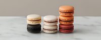 Colorful French macarons arranged in neat stacks on marble surface against neutral background, showcasing variety of flavors from chocolate to caramel and vanilla.