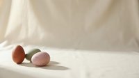 Three speckled Easter eggs in pastel pink, green, and terracotta tones arranged on a soft linen surface with warm natural light.