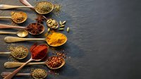 Colorful spices and herbs in wooden spoons arranged on dark slate background with copy space for culinary cooking and seasoning concepts.