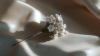 Elegant bridal hair pin with white flowers and pearls on soft fabric in natural sunlight for wedding accessories and romantic styling occasions.