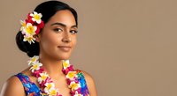 Young woman of South Asian descent wearing vibrant floral lei and colorful tropical dress against neutral background, perfect for travel, vacation, and summer holiday marketing campaigns.