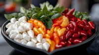 Fresh colorful mini sweet peppers and mozzarella balls arranged in rows on black plate with herbs, creating vibrant appetizer platter for party or catering.