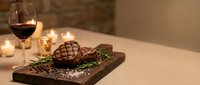 Grilled beef steak on wooden board with red wine glass and candles creating romantic dinner atmosphere for fine dining restaurant menu.