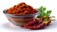 Red chili powder in glass bowl with fresh red chilies and parsley leaf on white background, aromatic spicy seasoning for cooking and food preparation.