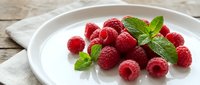 Fresh red raspberries with mint leaves arranged on white plate, ideal for food photography, healthy eating, dessert, and culinary content.