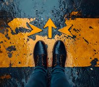 Black leather shoes standing at yellow directional arrows painted on dark asphalt ground, top view perspective showing decision making and future path choices.