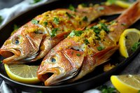 Fresh whole red snapper fish garnished with herbs, lemon slices and seasonings on cast iron pan, close up view of Mediterranean style seafood preparation.