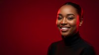 Young African American woman with bright smile wearing black turtleneck against red background for professional headshot and business portrait photography.
