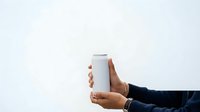 Cropped view of male hand holding blank white cylindrical container against neutral background for product mockup and branding purposes.