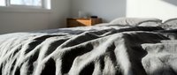 Unmade bed with rumpled linen sheets and blankets in neutral tones, bedroom interior with natural light from window, home comfort and relaxation concept.
