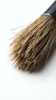 Natural bristle brush with black handle resting on white surface, showing detailed bristles and texture for art, craft, and painting projects.