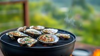 Fresh oysters grilling on barbecue with steam rising, topped with herbs and butter, served on round black grill outdoors against blurred natural background.