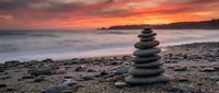 Zen stone stack on beach at sunset with dramatic orange sky and gentle waves creating peaceful meditation atmosphere for wellness and mindfulness concepts.