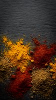 Colorful spice powders scattered on dark slate surface creating vibrant culinary composition for cooking and food preparation backgrounds.