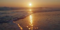 Golden sunlight reflects on wet sand as gentle waves roll onto shore during sunset, creating a peaceful and serene coastal landscape with warm orange tones.