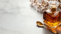 Amber glass bottle with golden liquid and decorative spoon on marble surface with dried flowers for luxury skincare, perfume, or wellness product packaging.