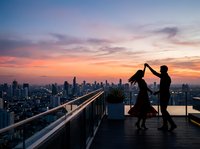 Silhouetted couple dancing on rooftop terrace at sunset with urban skyline, romantic evening celebration on high-rise balcony overlooking city lights.