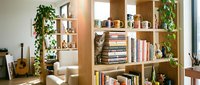 Modern wooden shelving unit with books, plants, and decorative items in bright living room space. Suitable for interior design, home decor, and lifestyle publications.