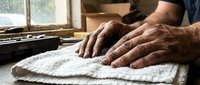 Senior craftsman hands working with white textured fabric in traditional workshop setting. Artisan textile production and handmade manufacturing process.