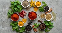 Colorful spices and herbs arranged in bowls on concrete surface. Fresh mint, turmeric, paprika, coriander seeds, cinnamon sticks create vibrant culinary display.