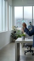 Man in business casual attire interacting with holographic data visualization display showing analytics charts and graphs in modern office workspace with natural light and potted plants.