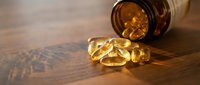 Golden omega-3 fish oil capsules spilling from amber glass bottle on wooden surface. Health supplement nutrition concept for wellness lifestyle.