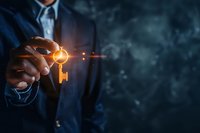 Businessman in dark suit holding glowing golden key with digital particles effect against blue background, representing success and business solutions.