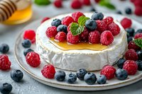 Baked brie cheese topped with honey, fresh raspberries, blueberries and mint leaves on gray plate. Close up view of gourmet appetizer with melted camembert.