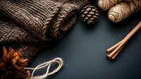 Cozy winter composition with knitted scarf, pine cones, cinnamon sticks and twine on dark background. Seasonal flat lay capturing warmth and comfort.