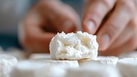 Fresh soft cheese with creamy texture and white color close up on light background, hands breaking piece to show delicate interior structure.