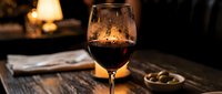Glass of red wine on wooden table with warm lighting and cozy fireplace background creating elegant dining atmosphere for restaurants and hospitality.