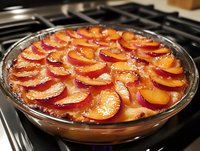 Fresh plum tart with overlapping sliced plums arranged in concentric circles on sweet custard filling in glass baking dish, homemade dessert preparation.