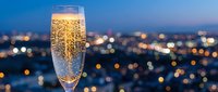 Champagne flute with golden bubbles against blurred city lights at dusk, luxury celebration concept for New Year, wedding, anniversary or special occasion.