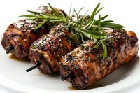 Grilled chicken rolls with fresh rosemary sprigs and herbs, glazed in savory marinade on white plate, close up view showing juicy texture and caramelized surface.