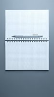 Open spiral notebook with grid paper and silver pen on gray background for office work and note taking.