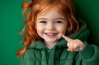 Happy redhead child girl wearing green hoodie smiling cheerfully against matching background for St Patrick Day celebration and seasonal campaigns.