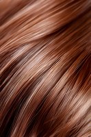Close-up macro shot of shiny brown hair strands showing texture and natural highlights, suitable for beauty and haircare advertising and marketing materials.