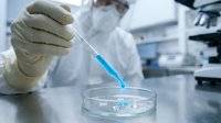 Laboratory scientist in protective equipment conducting chemical analysis with blue liquid sample in sterile research environment for medical testing.