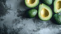 Fresh sliced avocados with pits displayed on dark textured surface, overhead flat lay composition for food styling, healthy eating, culinary content, and recipe design projects.