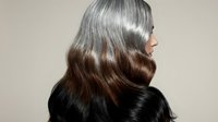 Young woman with glossy wavy brown hair showing healthy shine and movement against neutral background for beauty and haircare concepts.