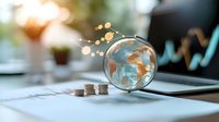 Glass globe with golden world map on financial documents and stacked coins, with rising graph line and bokeh lights, representing global business growth and investment.